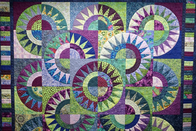 Quilt with green, blue, purple, and pink abstract sunburst pattern.